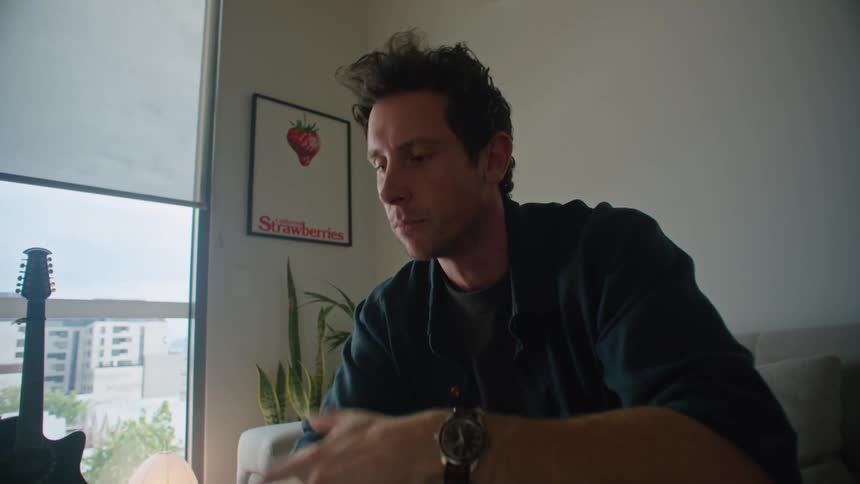 Man with black shirt watch and pants sits on couch making a video call on laptop in the living room at condo