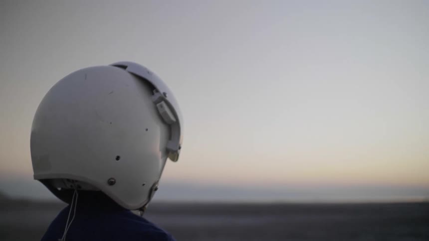 A young boy stands outside in a barren desert with a helmet on