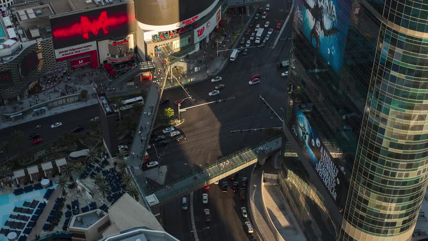Pedestrians move across a walkway bridge as traffic moves under them in a downtown area of a city