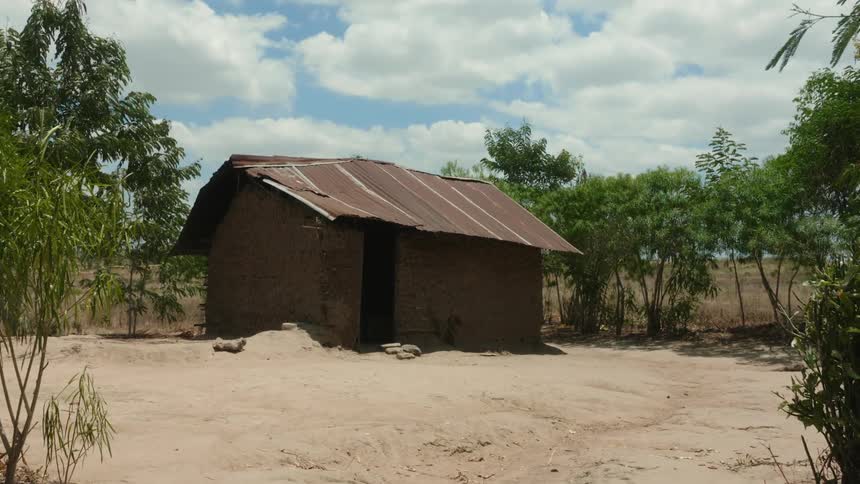 An old building stands in a rural area with a few trees around it under a cloudy sky