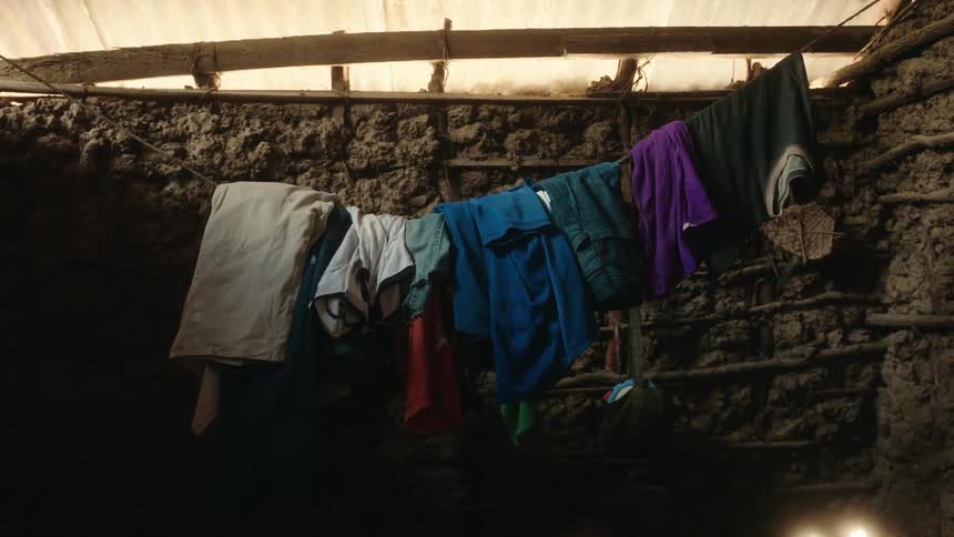 Clothes hanging on line inside a room with dirt walls and a corrugated fiberglass roof