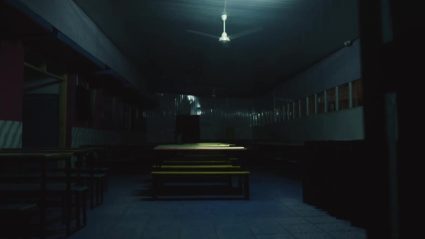 A light is on in a room filled with tables at the end of a hallway