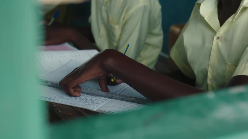Two students write on workbooks sitting at adesk