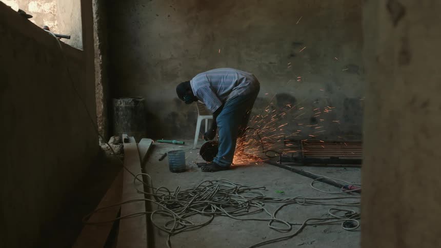 Man wearing protective gear creates a shower of sparks while sawing metal in unfinished building