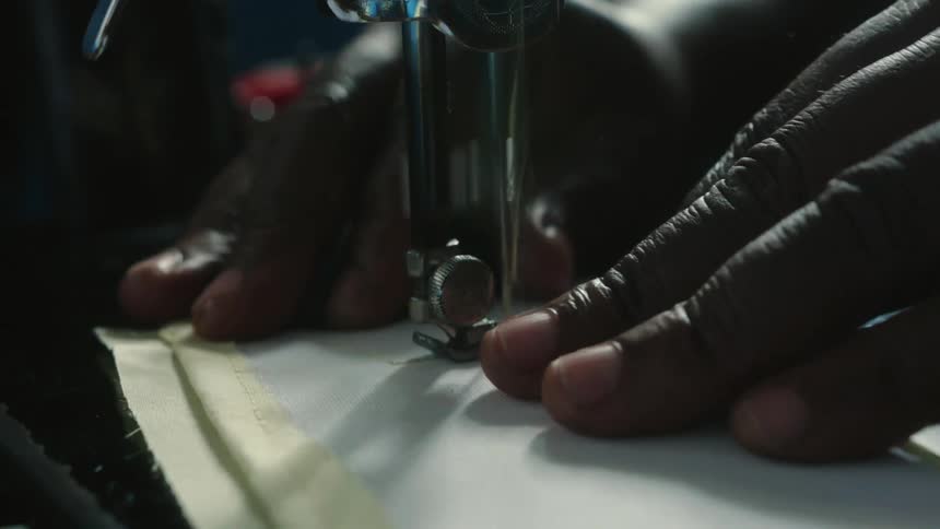 A person holds a small piece of fabric while using a sewing machine