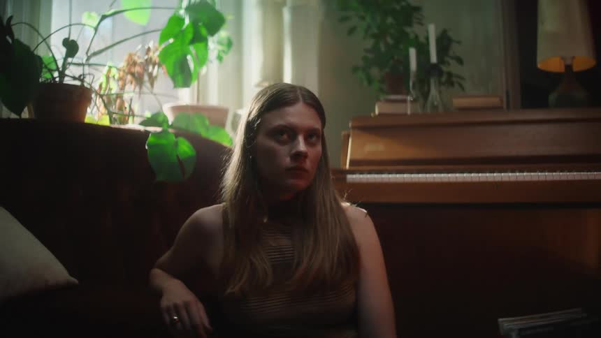 A woman is sitting on the floor near a piano instrument