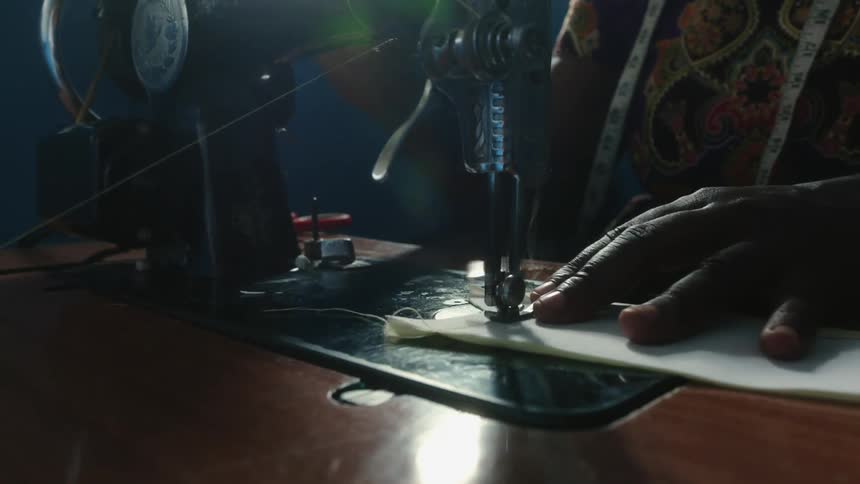 Woman uses sewing machine in dim lit room