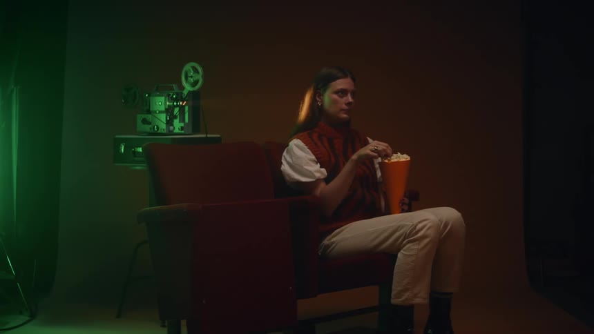 A woman sitting in a chair eating popcorn in front of a video camera displaying an image