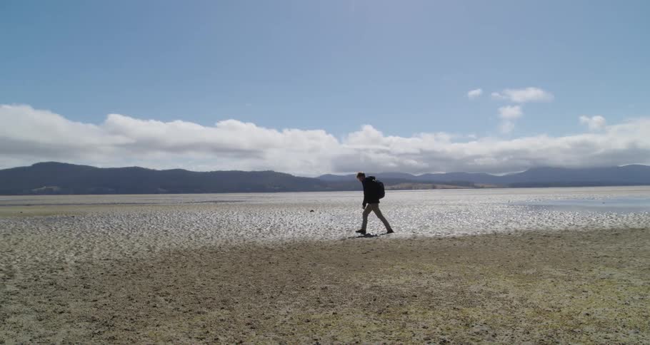 A man wearing a backpack walks along a wide open landscape