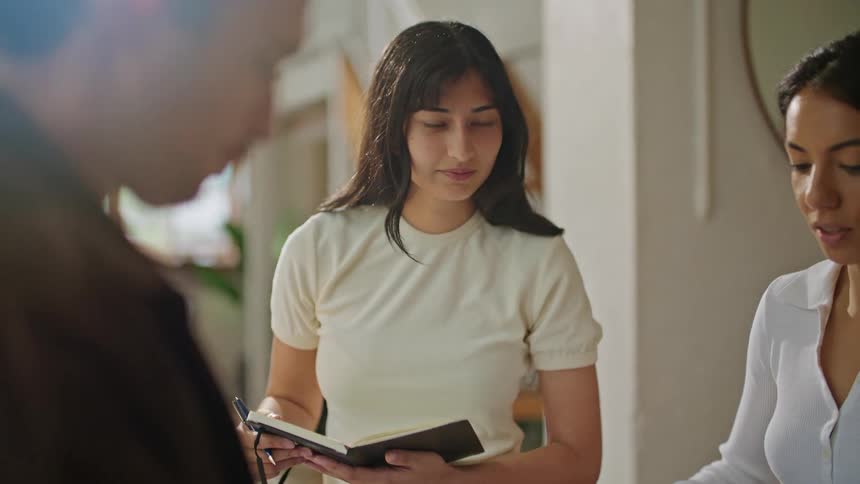 People stand in office having a discussion while one person holds notebook ready to take notes