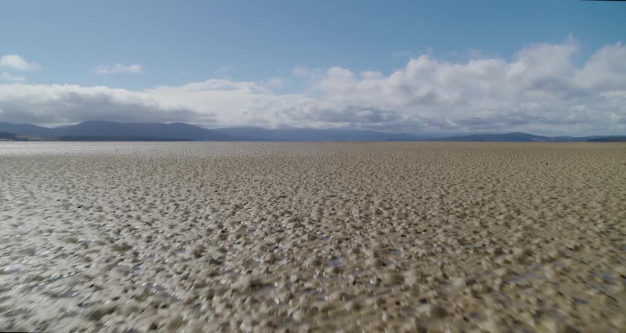 A time lapse of a drone view of wet sandy flats with mountains in the distance