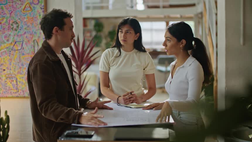 Man with mustache and brown jacket talks with women wearing white shirt at table