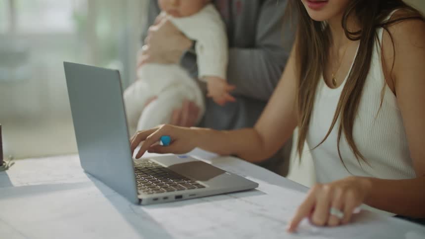 A man holds his baby while his wife tries to enter information on a laptop