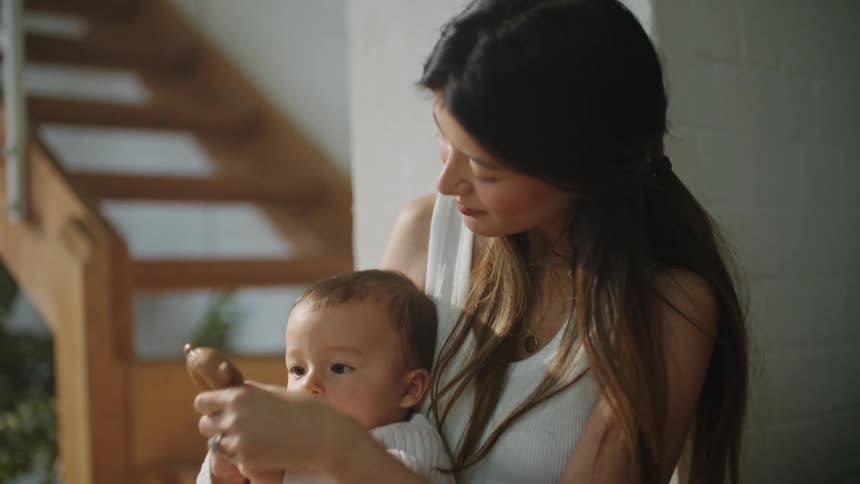 A mother holding her baby at home offers him a teething bear toy