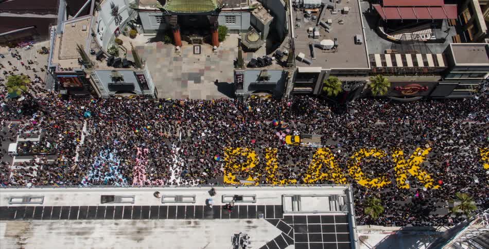 A large crowds stands on a black lives matter art installation on a city street