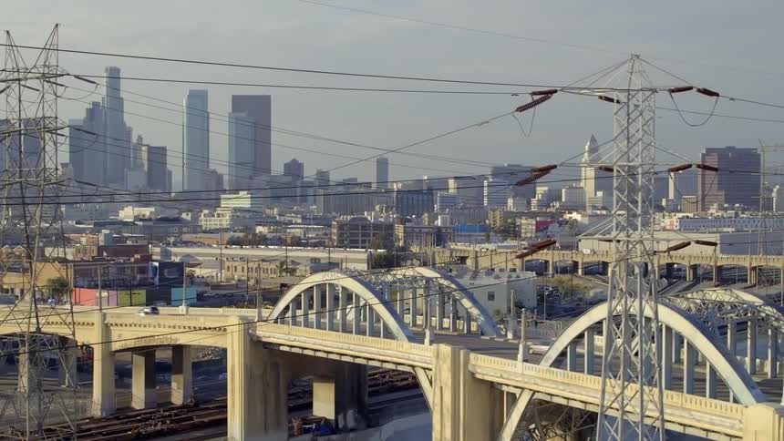 An aerial of a bridge going over train tracks with traffic traveling over the bridge going into a city