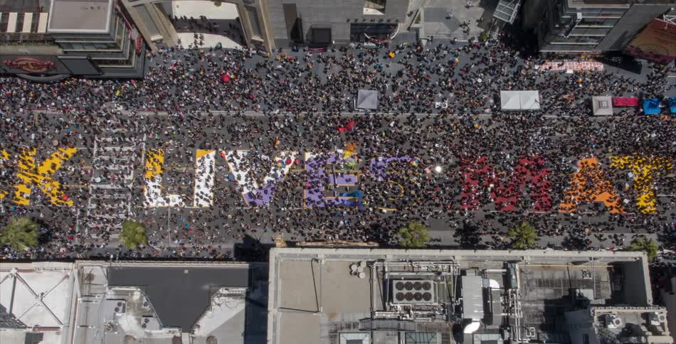 People crowd city street walking over large letters spelling the black lives matter slogan