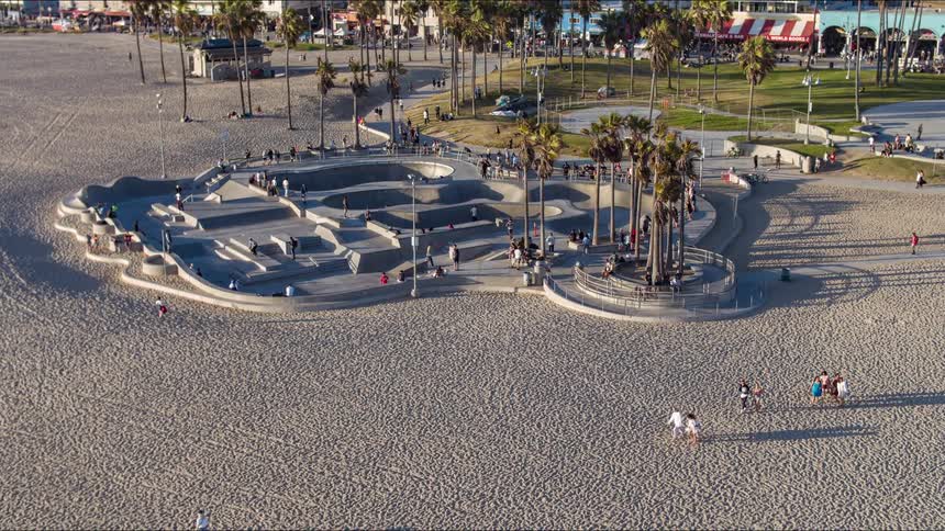People move along beach as others skateboard at skate park or move through park