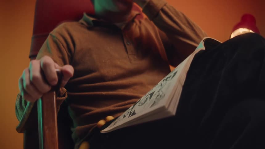 A man sitting in a chair with a book on his lap while he shovels a handful of food in his mouth