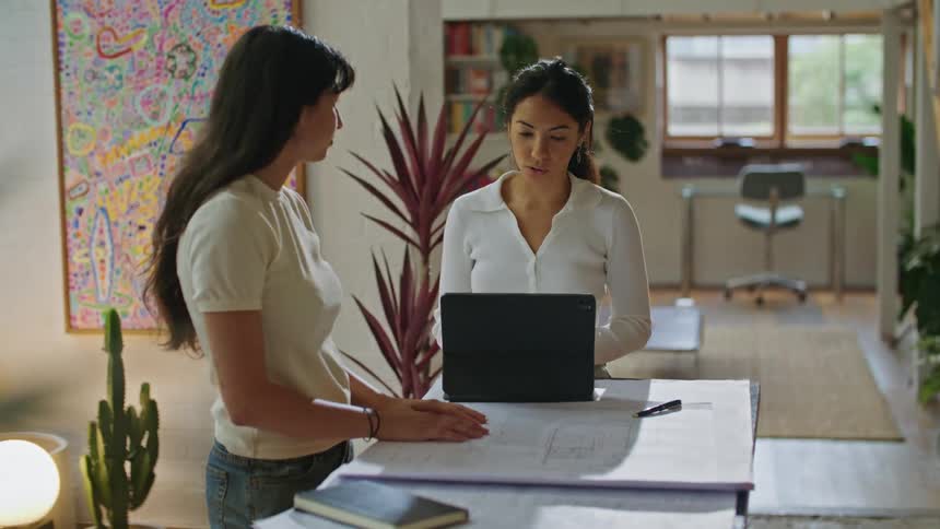 Women with white shirts and jeans work on plans and use tablet in room