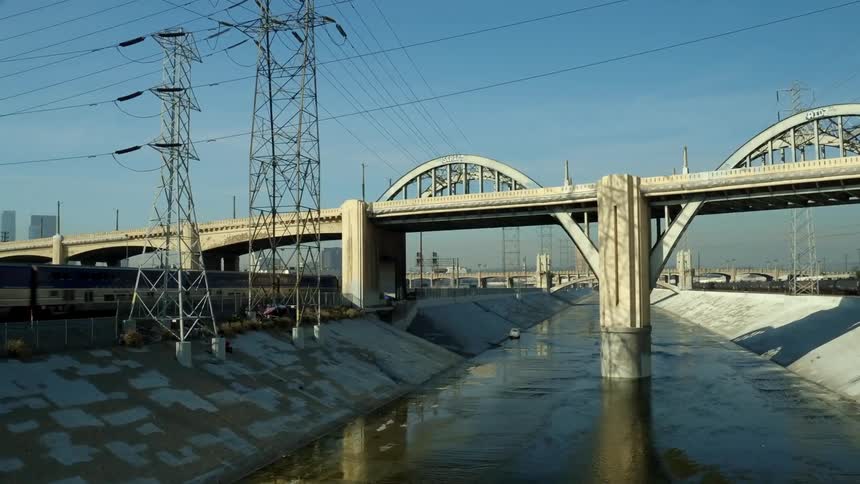 A drone view of a train going under a bridge next to an aqueduct with water in it
