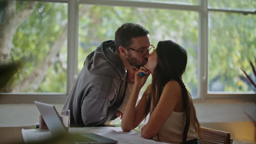 A woman works from a homebased office while her husband leaves the room with their child