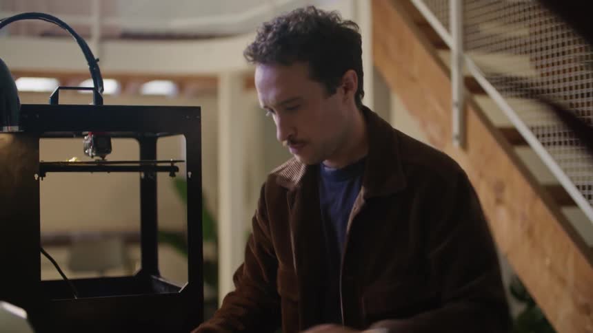 Man working with 3d printer moves along table to work with laptop