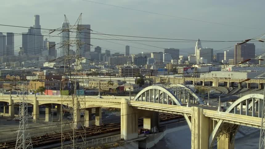 Traffic crosses bridge over railroad tracks with foggy city in the background under an overcast sky