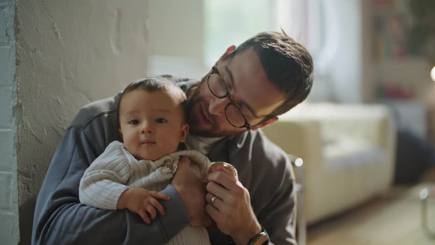 A father wearing glasses holds his infant son pointing upwards trying to get the babies attention