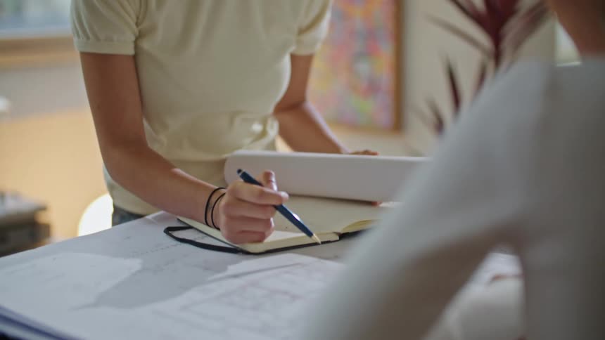 A woman talking to another woman across from her at a table with papers book and a pen in the womans hand