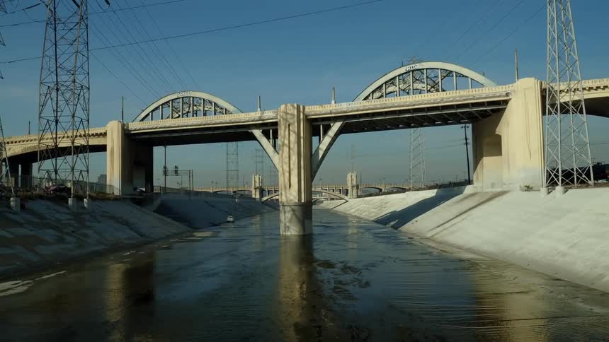 A drone view of an aqueduct with water in it and a concrete bridge going over it
