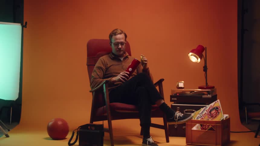 Man with glasses brown sweater and black pants sits in armchair and drops tennis balls in the studio