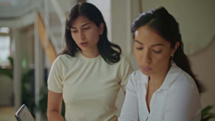 Two women discuss plan while one types onlaptop