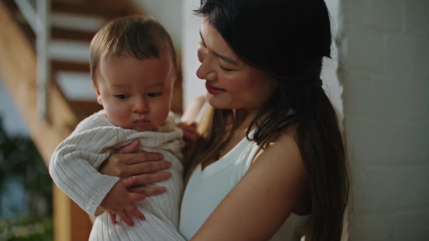 A woman is holding her infant baby indoors