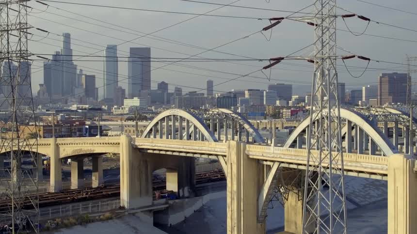 An aerial of a arched bridge going over a dry waterway with birds flying around and a dense city in the background