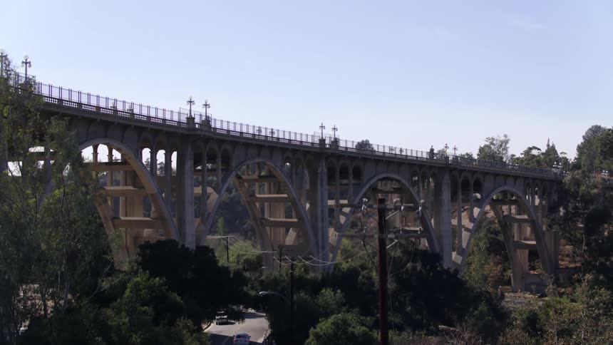 A drone view of a bridge going over a road with cars on it and trees and power lines underneath it
