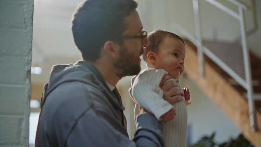A woman is sitting with a computer in her lap as she types and talks to her husband as he holds their baby