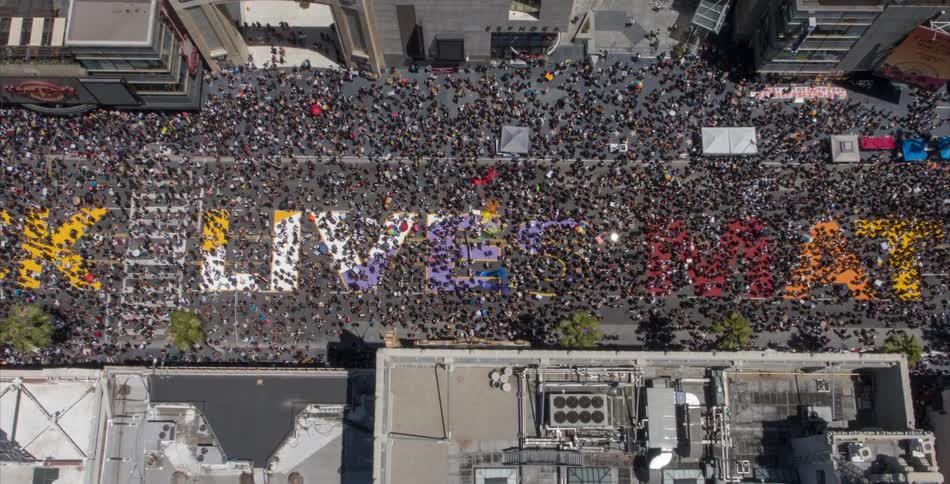 Aerial view of large crowd marching over all black lives matter mural on downtown street