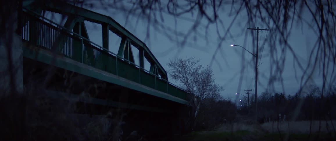 Street lights reflect on the surface of a flowing river under a bridge