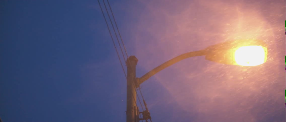 A close up view of some wires and poles and a light while it is snowing