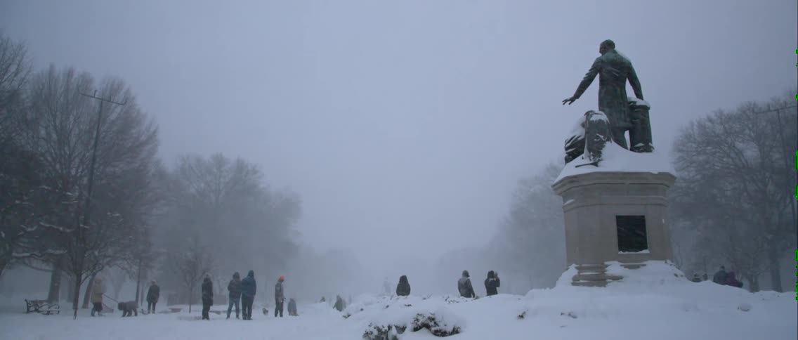A view of some people and animals outside playing in the snow while it is snowing