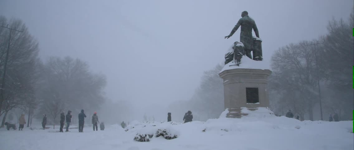 A group of people outside a building playing in the snow that is covering the ground
