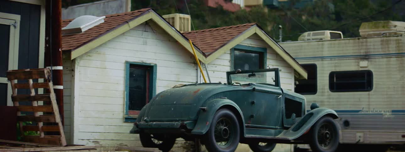 A vintage car and a trailer parked outside a small home
