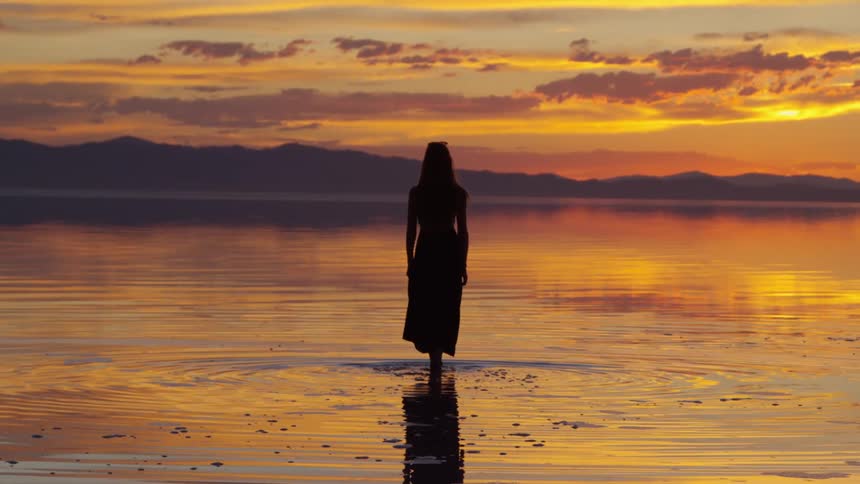 A woman is walking in the water at dawn