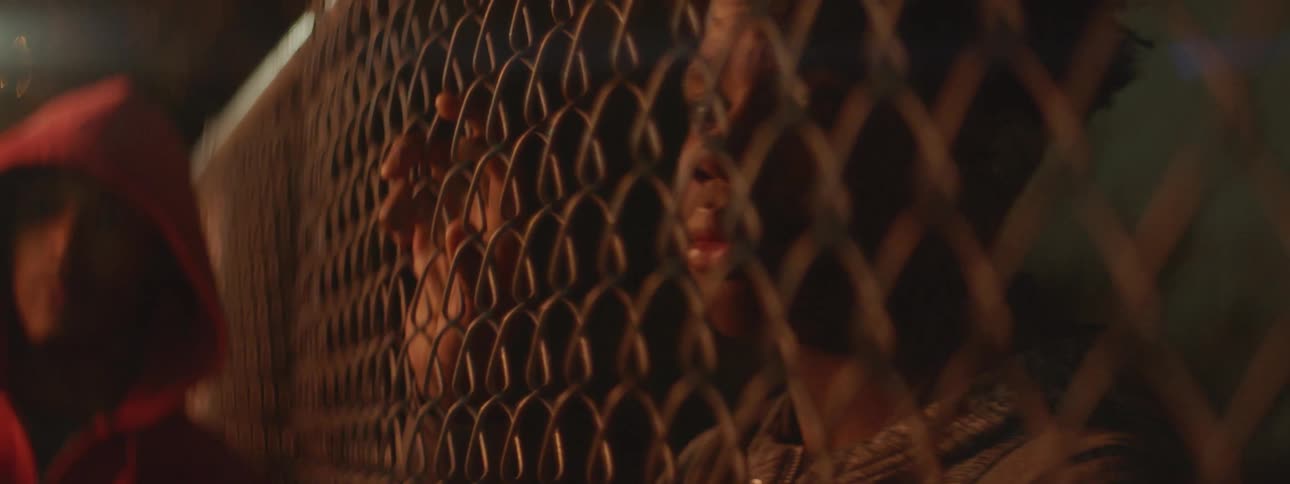 A boy leans against a fence at night
