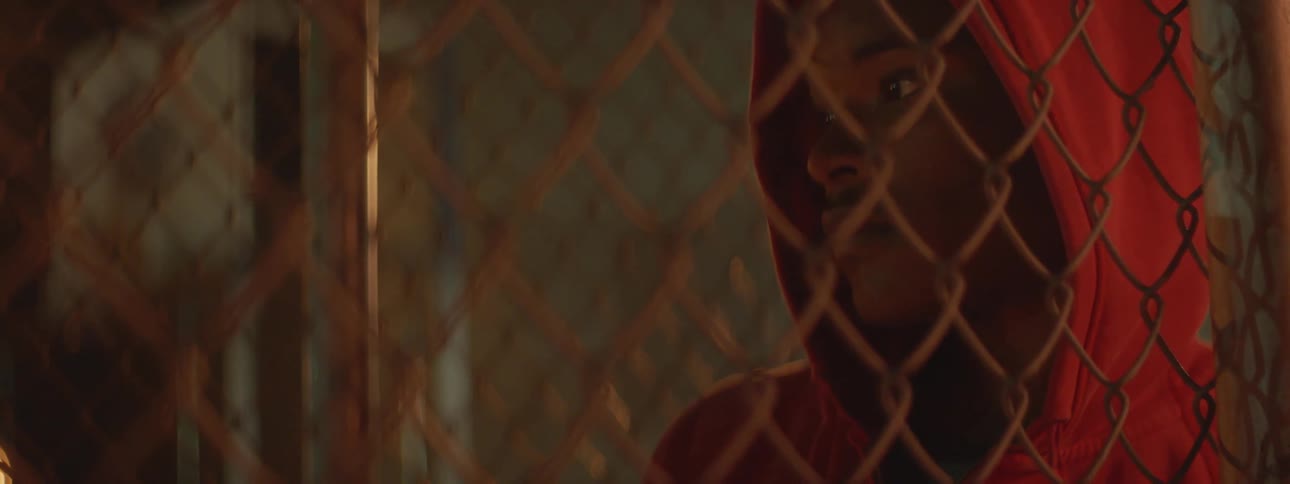 A man in an orange hoodie looks through a fence