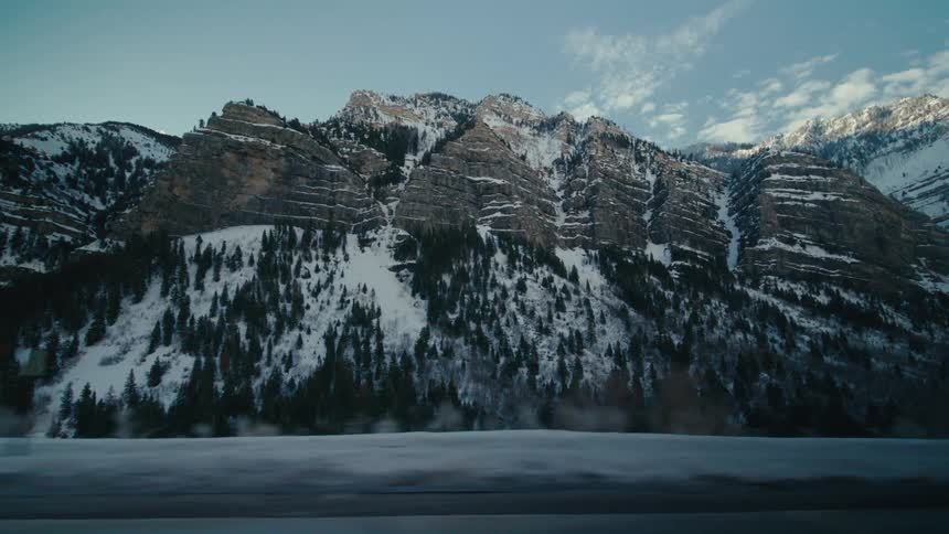 Vehicle drives on highway next to snowy mountain range