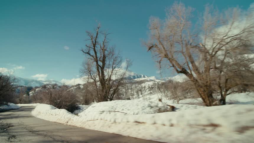 Traveling on a rural road lined with trees and mountains in the distance on a snowy winter day