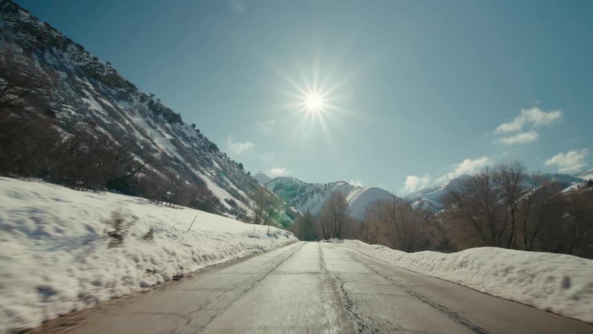 Traveling on a rural road lined with trees and mountains in the distance as the sun shines brightly on a snowy winter day
