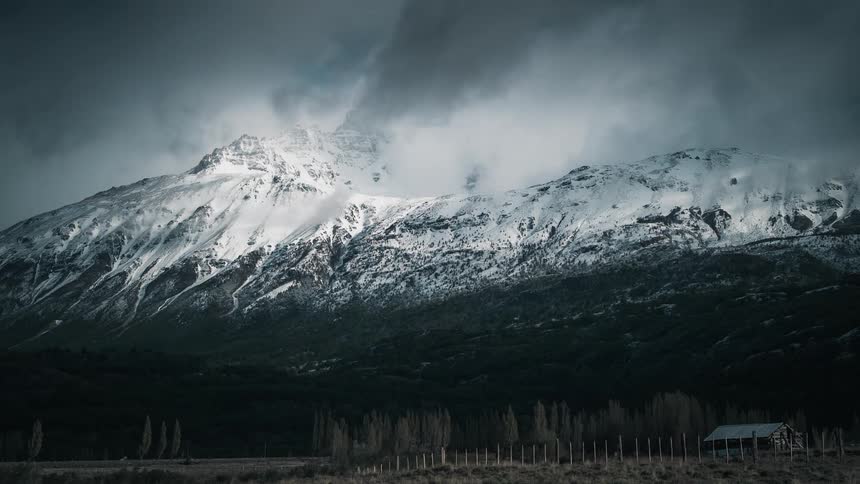Dark clouds move over a snow covered mountain in a rural area